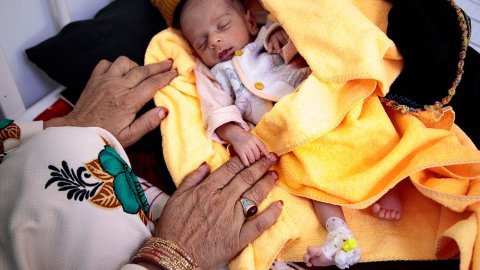 En liten bebis, som är inskriven på Läkare Utan Gränsers undernäringsklinik i Herat, Afghanistan, ligger på en gul filt. En kvinnas händer syns bredvid filten.