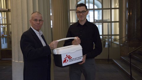 Två personer står bredvid varandra och håller i en kylbox för vaccin.