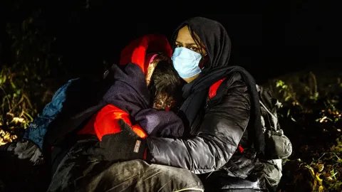 En mamma från Irak kramar sina döttrar, någonstans vid gränsen mellan Polen och Belarus