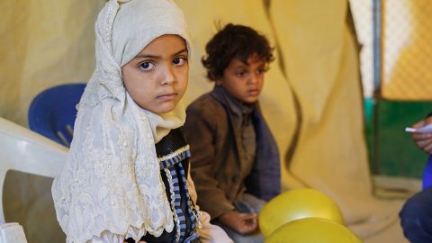 Sjuåriga Asifa sitter på en bänk, bakom henne sitter lillebror Wardan. De bor i ett flyktingläger i Marib, Jemen.