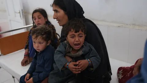 Han Bibi sitter på en säng på Boost sjukhus, Afghanistan, men sina tre små barnbarn.