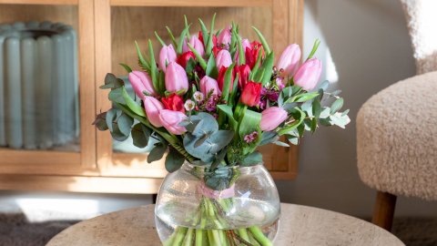 En bukett tuplaner i en glasvas på ett soffbord i ett vardagsrum med bokhyllor i bakgrunden