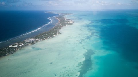 En smal landremsa med byggnader och träd på sig. Omkring ön är havet klarblått.