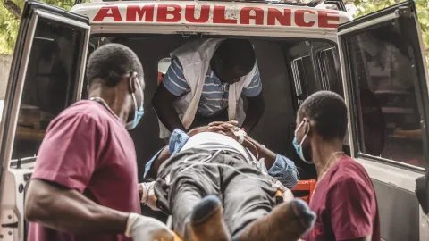 Två sjukhusklädda män bär in en person liggandes på en bår in i en ambulans