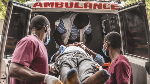 Två sjukhusklädda män bär in en person liggandes på en bår in i en ambulans