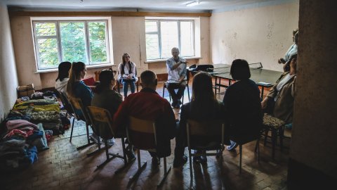 En grupp människor sitter på stolar i en ring. Två personer har på sig Läkare Utan Gränser västar.