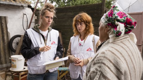 Två kvinnor i Läkare Utan Gränser västar pratar med en äldra kvinna. 