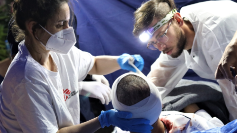 Patient  med bandage runt huvudet omges av sjukvårdspersonal.