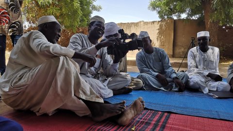 En grupp män sitter i en cirkel. En man håller i en videokamera.