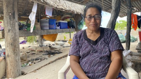 En kvinna sitter på en stol utanför sitt hus.