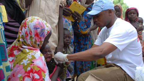 En man ger ett barn som sitter i en kvinnas knä en spruta.
