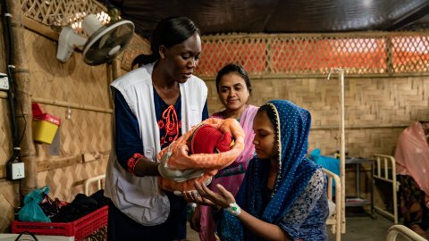En barnmorska räcker över ett barn till barnets mamma. 