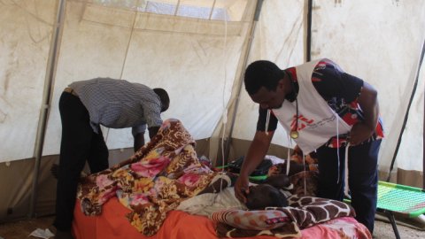 en patient ligger på en säng och omhändertas av personal på en vårdmottagning i ett flyktingläger i Tchad