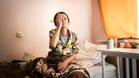 en kvinna sitter på en sjukhussäng och håller för ena ögat för ett syntest