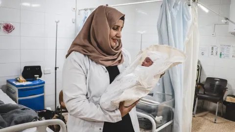 en barnmorska håller en nyfödd bebis insvept i vitt tyg på en mödravårdsavdelning