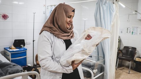 en barnmorska håller en nyfödd bebis insvept i vitt tyg på en mödravårdsavdelning