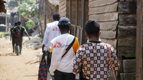 ett team från Läkare Utan Gränser går längs en bygata kantad av omålade trähus