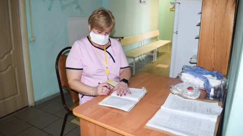 Kvinna i rosa t-shirt sitter vid skrivbord och antecknar i block.