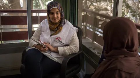 Kvinna med sjal och MSF-väst pratar med patient.