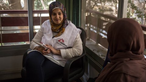 Kvinna med sjal och MSF-väst pratar med patient.