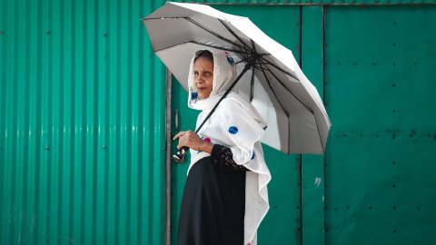 Kvinna går med paraply framför grön vägg.