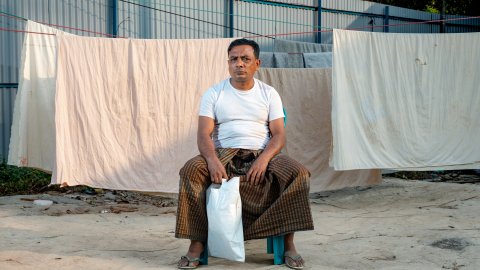 Man sitter på pall med hängande lakan bakom.