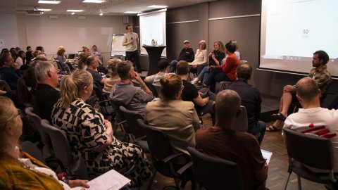 Mycket människor sitter i publik och tittar mot sex personer som pratar på scen.