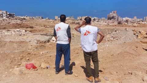 två män med vita västar tittar ut över raserade hus och gator i Derna 