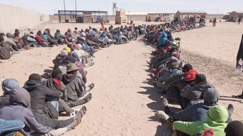 Hundratels personer sitter i tre långa köer framför en grind.