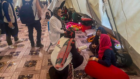 I ett tält sitter ett par kvinnor på golvet. Bredvid står Läkare Utan Gränsers personal på huk.