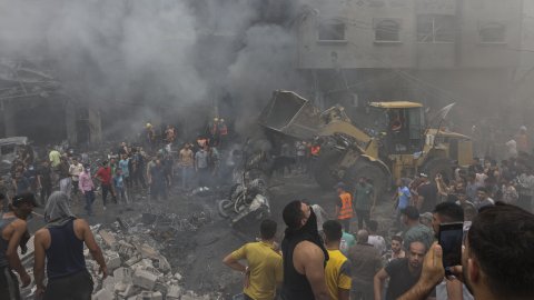 människor och en grävmaskin på en gata med sönderbombade byggnader