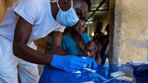 En manlig sjuksköterska men munskydd och plasthandskar undersöker ett malariatest på ett blått bord