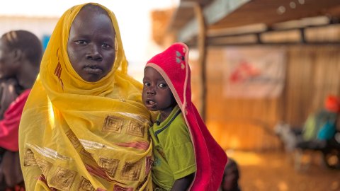 Kvinna håller sitt barn i famnen, kollar in i kameran.