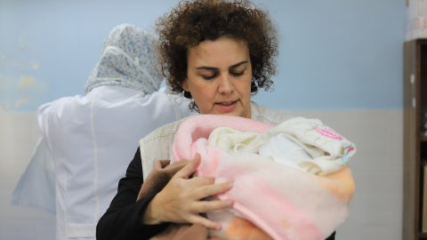 En kvinnlig barnmorska håller ett nyfött barn i en filt. 