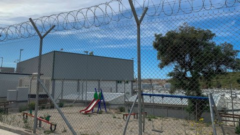 En byggnad som omringas av taggtråd. Innanför stängslet syns en lekpark för barn. 