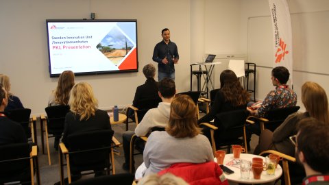 En man står vid en TV-skärm framför en publik och håller ett fördrag