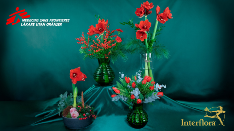 Fyra julblomsterarrangemang står uppställda i grupp mot en mörkgrön bakgrund