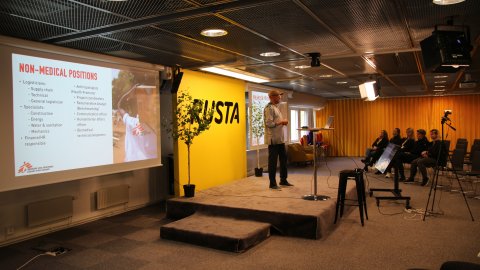 Man står på scen och i bakgrunden syns Rustas logotyp och Läkare Utan Gränsers presentation.