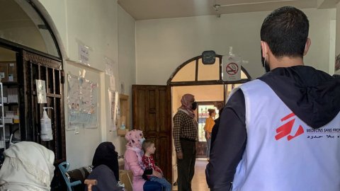 Ryggtavla av MSF-anställd omringad av patienter på en klinik.