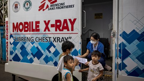 Två vuxna och ett barn står utanför Läkare Utan Gränsers mobila klinik.