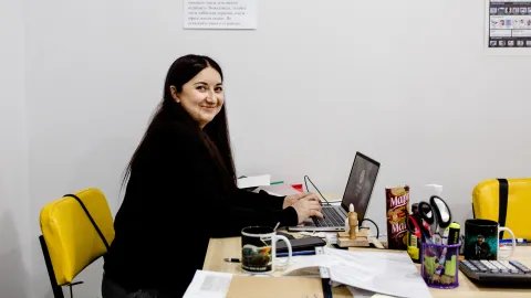 Kvinna sitter vid datorn och tittar in mot kameran och ler.