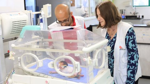 En bebis i en kuvös. Två från läkare utan gränser står och tittar in.