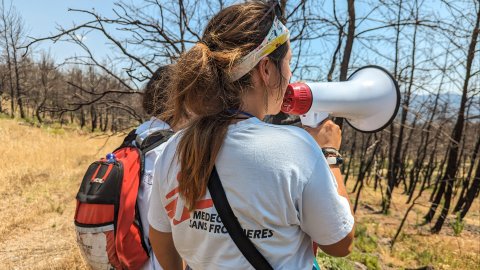 Ryggen på en Läkare Utan Gränser anställd som ropar ut i en megafon mot en tunn skog. 