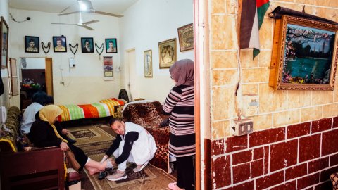 En Läkare Utan Gränser-anställd sitter på huk i ett vardagsrum och håller upp en kvinnas fot i sin hand för undersökning.