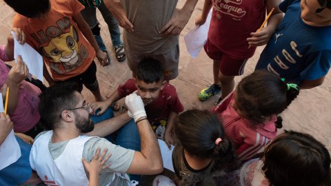 en grupp barn står i ring runt ett bord där en man ger en pojke en ansiktsmålning