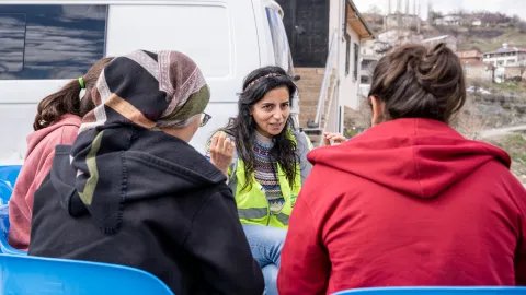 En grupp kvinnor, varav en har gul väst, sitter utomhus och pratar.