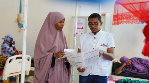 En man i Läkare Utan Gränser-väst visar ett papper för en kvinna.