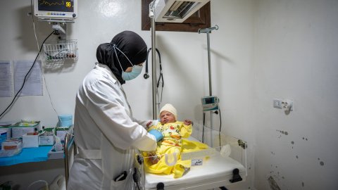 en sjuksköterska håller upp en nyfödd bebis som ligger på en sjukhusavdelning för nyfödda