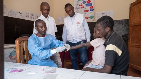 En laboratorieassistet tar ett blodprov under överinseende av sina handledare