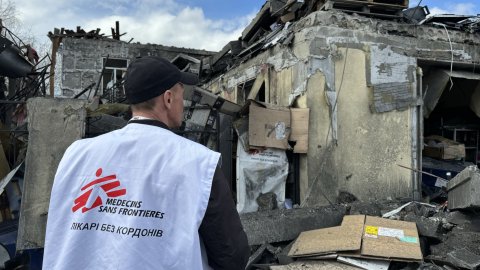 Man står med Läkare Utan Gränser-väst mot en byggnad som raserat.